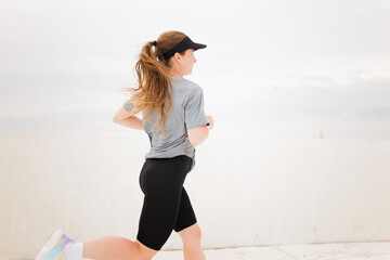 Young Woman Enjoying a Refreshing Morning Run Along a Scenic Waterfront Path Under a Cloudy Sky