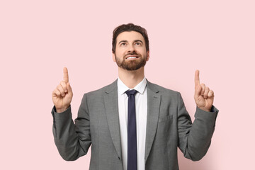 Young businessman pointing up on pink background