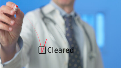 Doctor is drawing a red check mark in a checkbox with the word cleared written next to it,...
