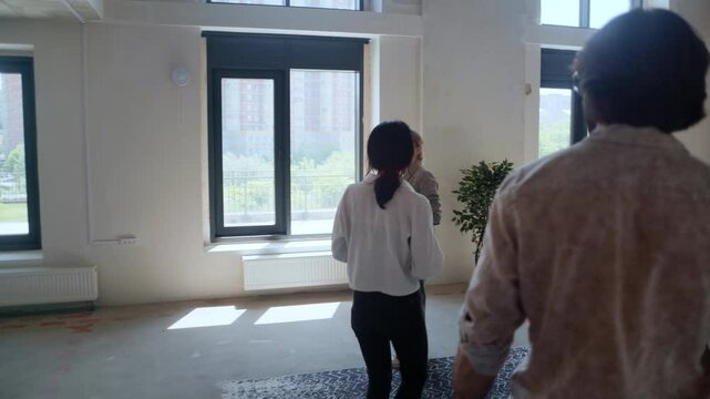 A young couple enters a modern flat with their realtor, beginning a home tour as the agent introduces key features of the apartment for potential purchase