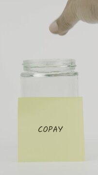 Copay concept with a hand inserting a coin into a glass jar labeled with a yellow sticky note. Set against a clean white background in vertical screen format, symbolizing savings for medical copay
