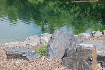 close-up stone blocks and wood chips forming the shoreline of a manmade pond in bright summer...