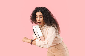 Shocked African-American woman with folders looking at wristwatch on pink background. Time...