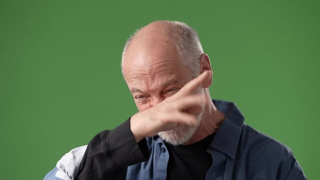 A middle-aged man shows a playful, exaggerated facial expression while sticking out his tongue in front of a green screen. The setting suggests humor.