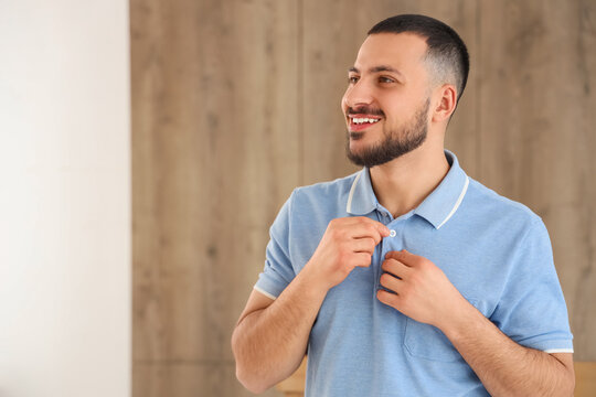 Young man buttoning up blue polo shirt at home