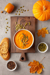 Creamy pumpkin soup topped with seeds, surrounded by dried fall leaves, rustic bread slices, whole...