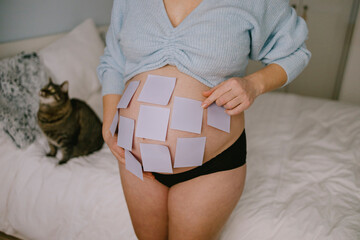 Pregnant Woman with Sticky Notes on Belly, Expecting Baby, Creative Maternity Concept with Cat in Background