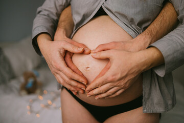 Pregnant couple forming heart shape on belly with hands – tender maternity moment at home