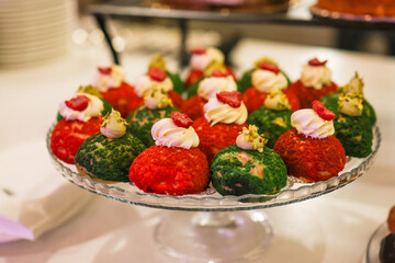 Dolci monoporzione rossi e verdi guarniti con panna montata e frutta fresca serviti ad un buffet di dolci di un matrimonio
