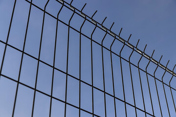 a thin metal lattice fence against a blue sky background, a small thin fence dividing the territory