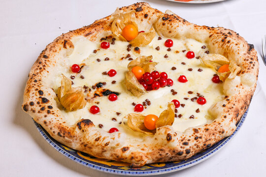 Pizza tradizionale napoletana servita con ricotta dolce, gocce di cioccolato, mango e ribes in una pizzeria 