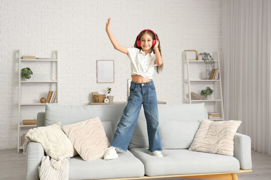 Fototapeta Cute girl in headphones dancing on sofa at home