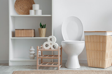 Interior of light restroom with toilet bowl, shelf unit and basket