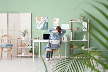 Young woman sitting at table in office, back view