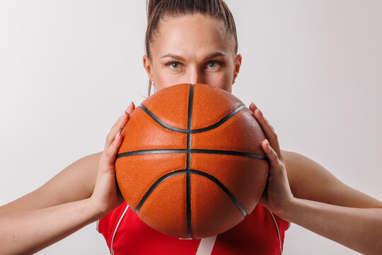 Focused Female Basketball Player in Red Jersey Holding Ball Close to Face, Isolated Studio Portrait
