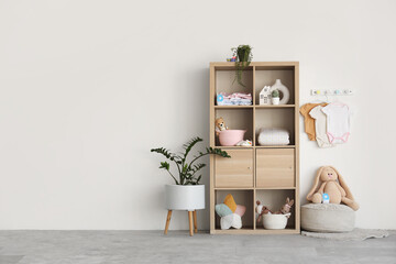 Interior of stylish children's room with shelving unit, toys and baby clothes hanging on light wall