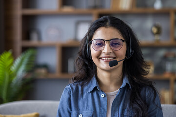 Close-up portrait of a young Indian girl in headphones and a headset at home, looking and smiling at the camera