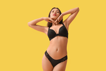 Beautiful young Asian woman in sexy black underwear on yellow background