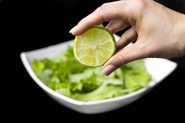 Hand squeezing half of a fresh lime on a black background