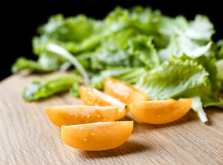 Close-up of tomatoes and lettuce on a wooden board on a black background. Concept of healthy eating and organic farm products