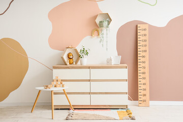 Interior of modern children's room with wooden stadiometer, toys and houseplants on commode