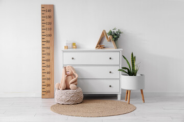Interior of children's room with wooden stadiometer, houseplants and toys on commode