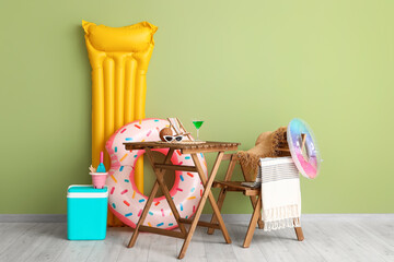 Inflatable mattress with ring, beach cooler, cocktail and summer accessories on table near green...