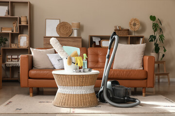 Bucket of cleaning supplies and brushes with vacuum cleaners on table in living room