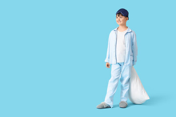 Cute boy in pajamas with pillow on blue background