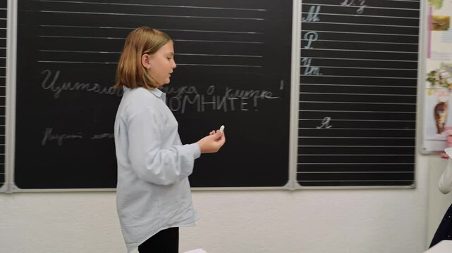 Close-up of girls in classroom, one holding chalk, other observing. Back to school atmosphere. Focus on participation, discipline, education, handwriting, and learning in bright school room