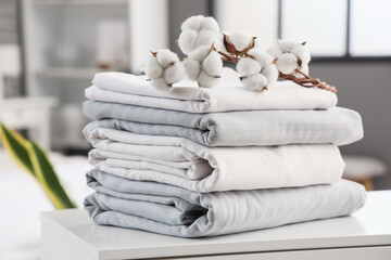 Stack of clean bed sheets with cotton flowers sprig on table in bedroom