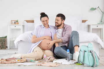 Happy pregnant couple packing maternal hospital bag in bedroom