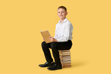 Cute little boy sitting on stack of books against color background