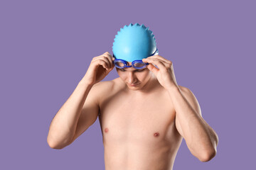 Male swimmer putting on goggles against purple background