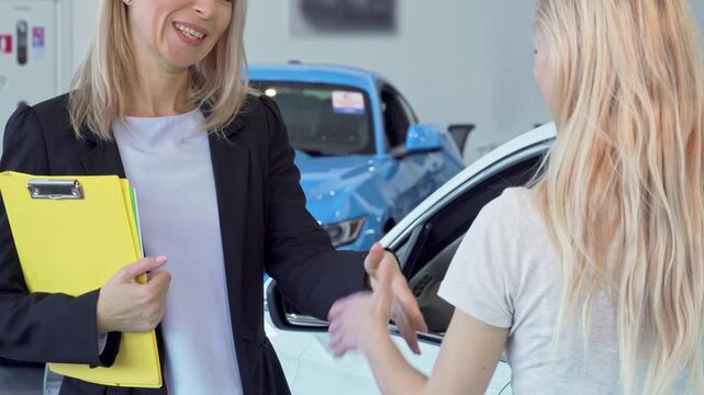 Excited female customer receiving car keys while shaking hands with a professional saleswoman
