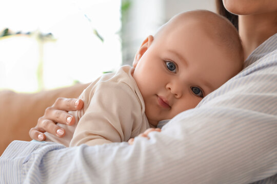 Beautiful young happy mother hugging her cute little daughter on sofa at home