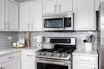 Fototapeta premium A kitchen detail with white cabinets and countertops, grey subway tile backsplash, stainless steel appliances, and decorations on the countertop.