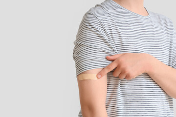 Young man pointing at applied medical patch on white background, closeup. Vaccination concept