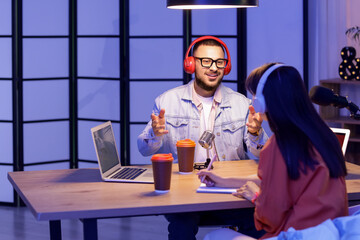 Young man with headphones talking to podcaster in studio
