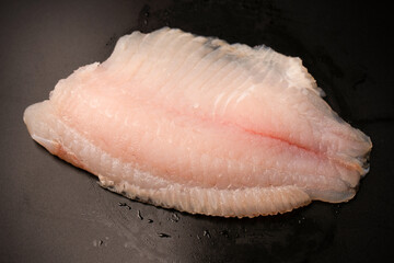 Fresh tilapia fillet on black background, top view.