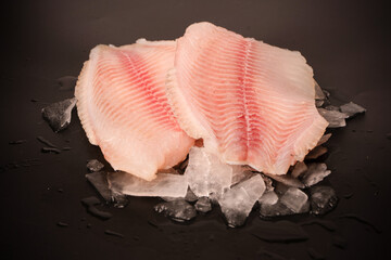 Fresh tilapia fillet on ice on black background