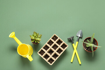 Seed tray with soil, potted plants and gardening tools on green background
