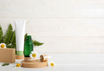 Composition with plaster stands, chamomile flowers, bottle and tube of cosmetic products on white wooden background