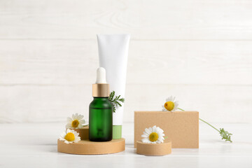 Composition with plaster stands, chamomile flowers, bottle and tube of cosmetic products on white wooden background