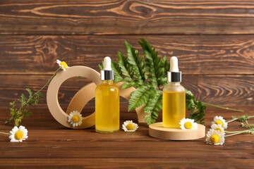 Bottles of cosmetic products, plaster stands and chamomile flowers on wooden background, closeup