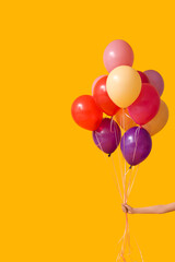 Female hand with colorful air balloons on orange background