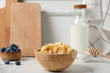 Bowl with tasty cornflakes, blueberries and bottle of milk on light background