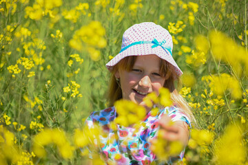 Happy child with pink hat offering yellow flowers in a canola field during a sunny summer day