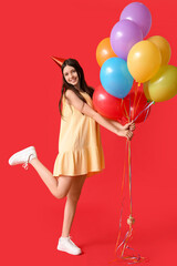 Beautiful teenage girl in party hat with colorful air balloons on red background