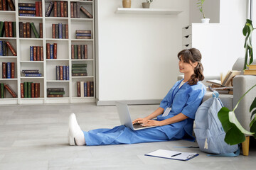 Female medical intern studying with laptop on floor in library